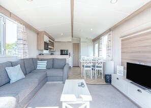 A modern living room with a sofa, coffee table, TV, and a kitchen in the background. - Tweed Retreat - 2 Bedroom (Pet Friendly) (Coldstream)