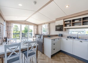 A modern kitchen with a built-in oven, a dining area with a table and chairs, and a view of the outdoors through large windows.