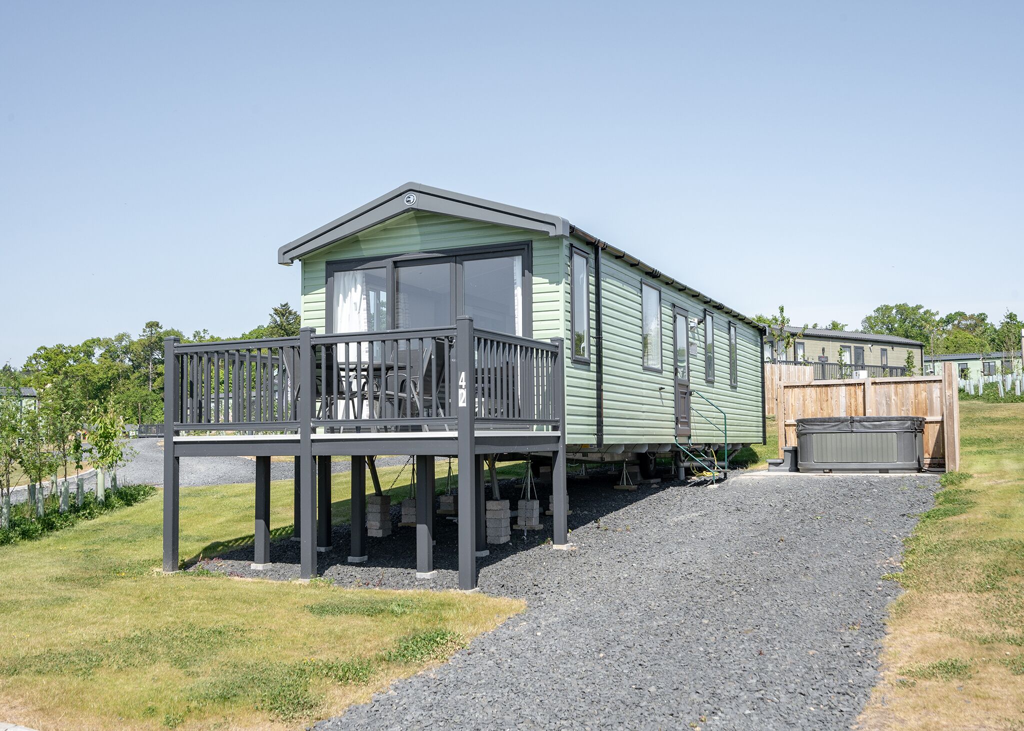 A mobile home with a deck, a covered outdoor area, and a gravel driveway.