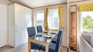 A dining area with a glass table, blue chairs, and yellow curtains. - Cheviot Retreat - 2 Bedroom (Pet Friendly) (Coldstream)