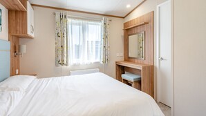 A bedroom with a bed, a bedside table, a mirror, a window with curtains, and a radiator. - Cheviot Retreat - 2 Bedroom (Pet Friendly) (Coldstream)