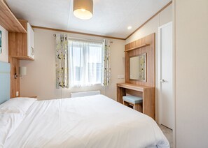 A bedroom with a bed, a bedside table, a mirror, a window with curtains, and a radiator. - Cheviot Retreat - 2 Bedroom (Pet Friendly) (Coldstream)