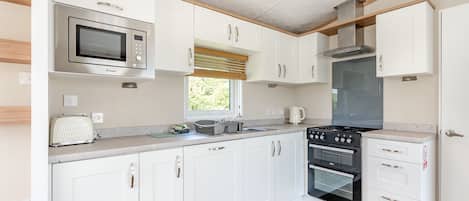A modern kitchen with white cabinets, a microwave, a stove, and a window.