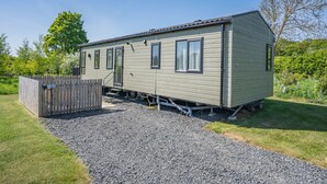 A single-story mobile home with a fenced yard, a gravel driveway, and a small shed. - Cheviot Retreat - 2 Bedroom (Pet Friendly) (Coldstream)