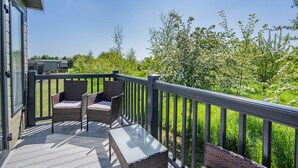 A deck with wicker furniture and a glass table, overlooking a garden with trees and a building in the background. - Cheviot Retreat - 2 Bedroom (Pet Friendly) (Coldstream)