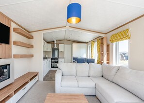 A modern living room with a sectional sofa, a TV, wooden shelves, and a kitchen in the background. - Cheviot Retreat - 2 Bedroom (Pet Friendly) (Coldstream)