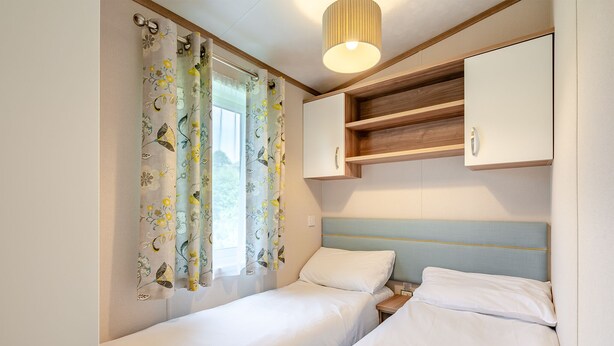 A bedroom with two single beds, a window with floral curtains, a wooden headboard, and a bedside table. - Cheviot Retreat - 2 Bedroom (Pet Friendly) (Coldstream)