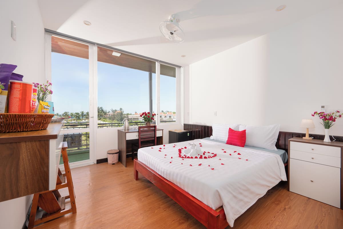 A modern hotel room with a large bed, a desk, and a view of the outdoors.