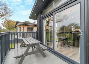 A modern outdoor deck with a picnic table and a glass door leading to a patio area.