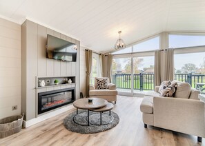 A living room with a fireplace, a television, a round coffee table, and a sofa. - Family friendly lodge. (Swinethorpe, Nr Lincoln)
