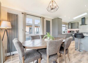 A modern kitchen with a central island, a dining area with a round table and cushioned chairs, and a large window with curtains.