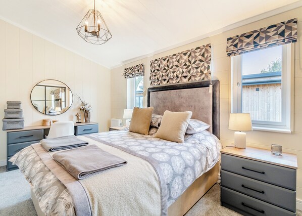 A bedroom with a bed, bedside tables, a mirror, a window with curtains, and a hanging light fixture.