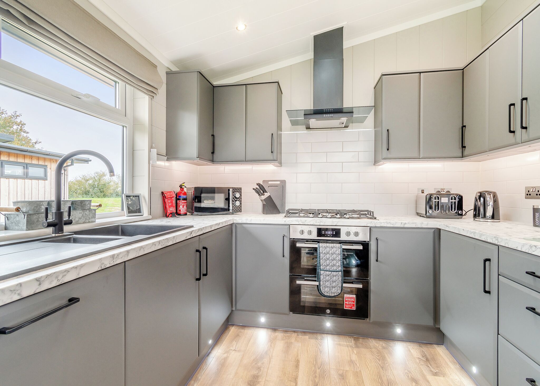 Una cucina moderna con pensili grigi, un piano cottura in acciaio inossidabile, forno integrato e un'ampia finestra.