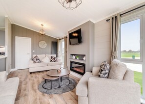 Ein modernes Wohnzimmer mit Sofa, Couchtisch, Kamin, Fernseher und großen Fenstern.