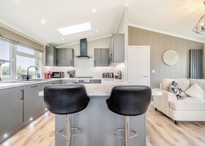 Una cocina moderna con una isla central, taburetes de bar, un sofá y un reloj en la pared.