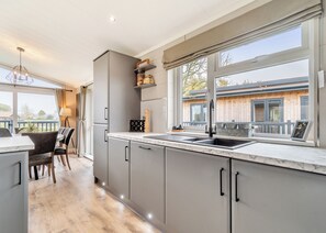 A modern kitchen with a large window, a dining area with a table and chairs, and a view of a building outside. - Family friendly lodge. (Swinethorpe, Nr Lincoln)