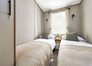 A compact room with two beds, a small table, and a window with curtains.