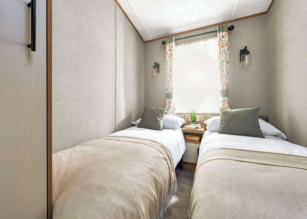 A compact room with two beds, a small table, and a window with curtains.