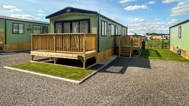 A mobile home with a wooden deck, a small front porch, and a grassy yard. - Platinum Caravan (Pet) (Bedale)