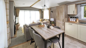 A modern kitchen with a wooden table, grey chairs, and a coffee maker. - Platinum Caravan (Pet) (Bedale)