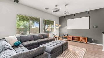 Un salon moderne avec un canapé d’angle, un pouf et un grand téléviseur à écran plat fixé au mur.