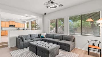 Un salon moderne avec un canapé d’angle, un pouf et un coin repas doté de meubles de rangement en bois.