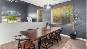 Un coin repas avec une table et des chaises en bois, une plante en pot et une fenêtre avec des stores.