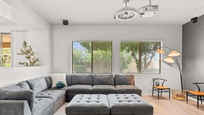Un salon moderne avec un canapé d’angle, un pouf et une lampe sur pied.