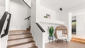 Un escalier avec des marches en bois et des rampes noires, menant à un mur blanc orné d’une étagère et d’une plante en pot.