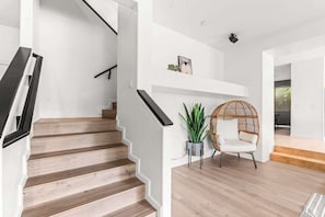 A staircase with wooden steps and black handrails, leading to a white wall with a shelf and a potted plant.