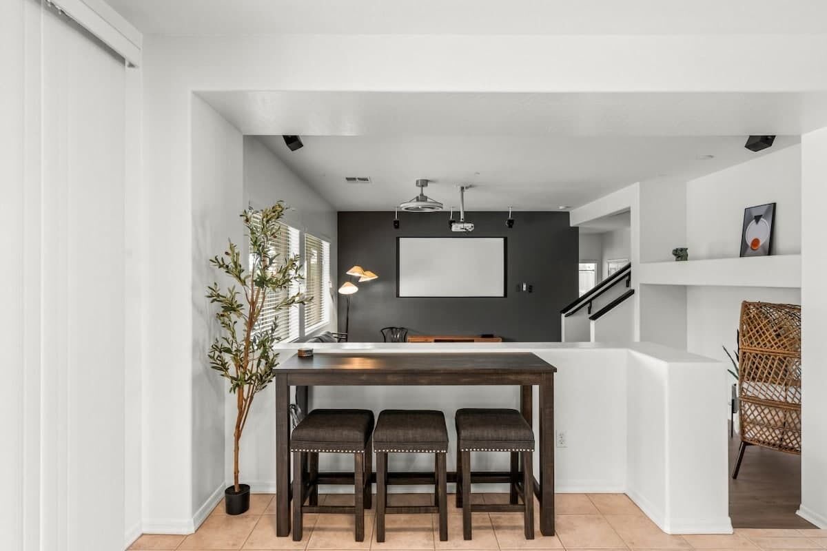 Une cuisine moderne avec un revêtement mural foncé, un plan de travail blanc et trois tabourets.