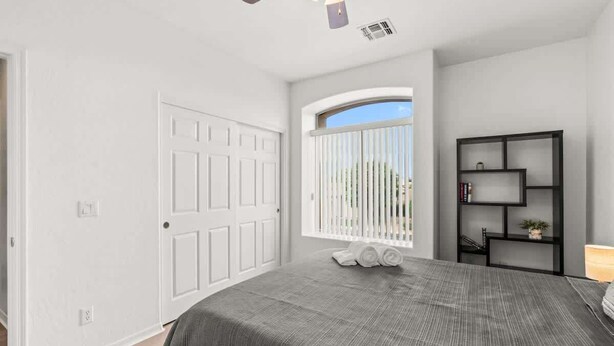 Une chambre à coucher avec un lit, une fenêtre avec des stores, un ventilateur de plafond et une bibliothèque noire.