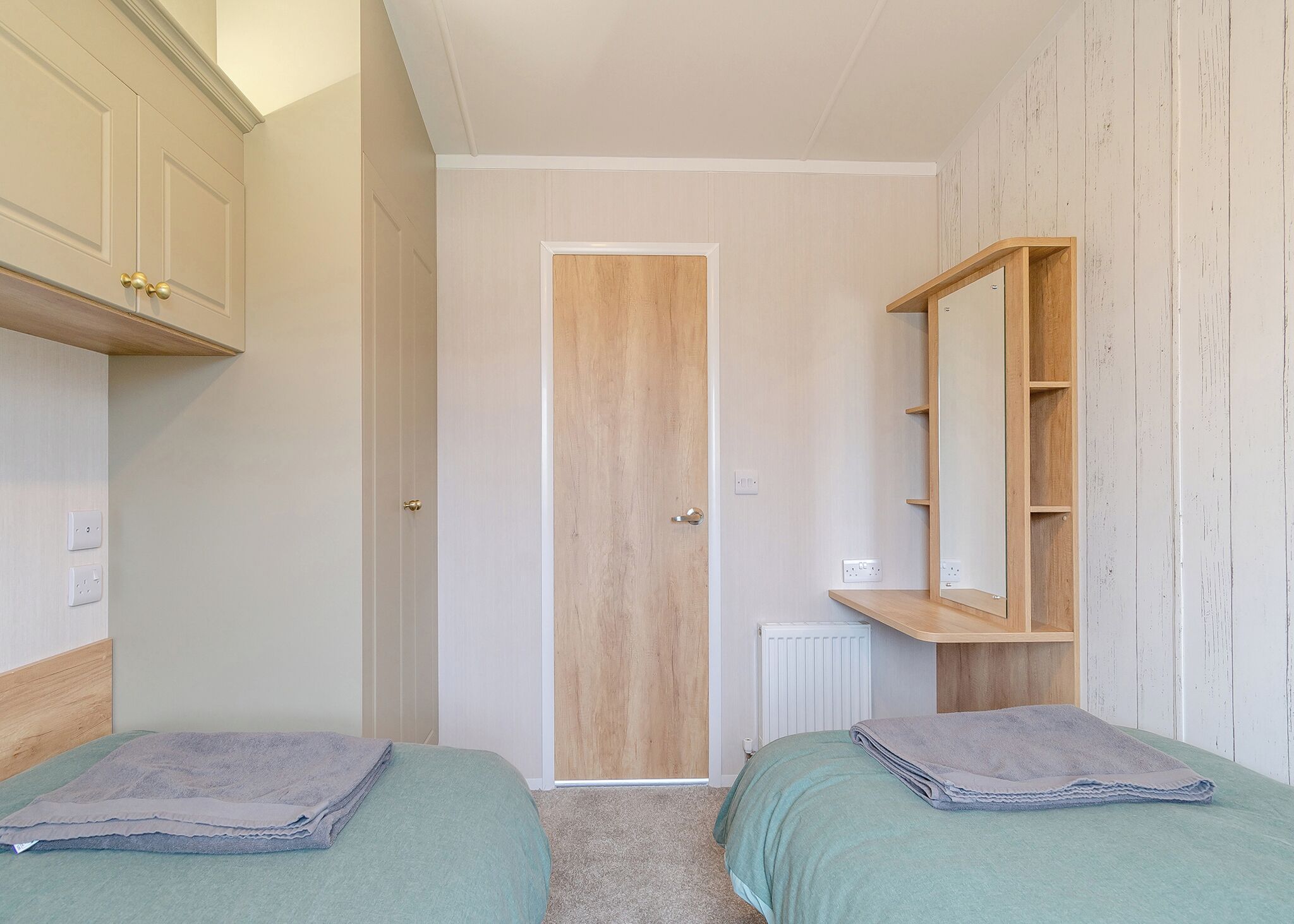 A bedroom with two beds, a wooden wardrobe, a mirror, and a radiator.