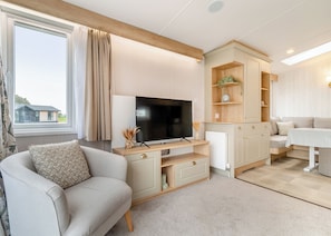 Ein modernes Wohnzimmer mit Flachbildfernseher, einer Couch, einem Essbereich und Blick auf ein Haus durch ein Fenster.