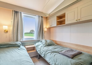 A bedroom with two single beds, a window with curtains, a bedside table, and a wardrobe. - Family and dog friendly lodge. (Swinethorpe, Nr Lincoln)