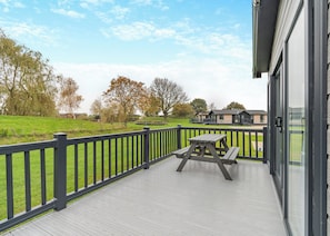 A wooden deck with a picnic table, a black railing, and a view of a building and trees in the background.
