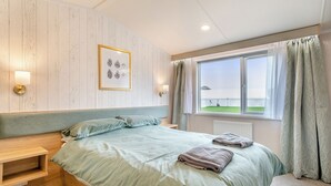 Et soveværelse med en seng, et natbord, et billede i ramme på væggen og et vindue med gardiner.