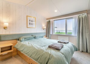 A bedroom with a bed, a bedside table, a framed picture on the wall, and a window with curtains.