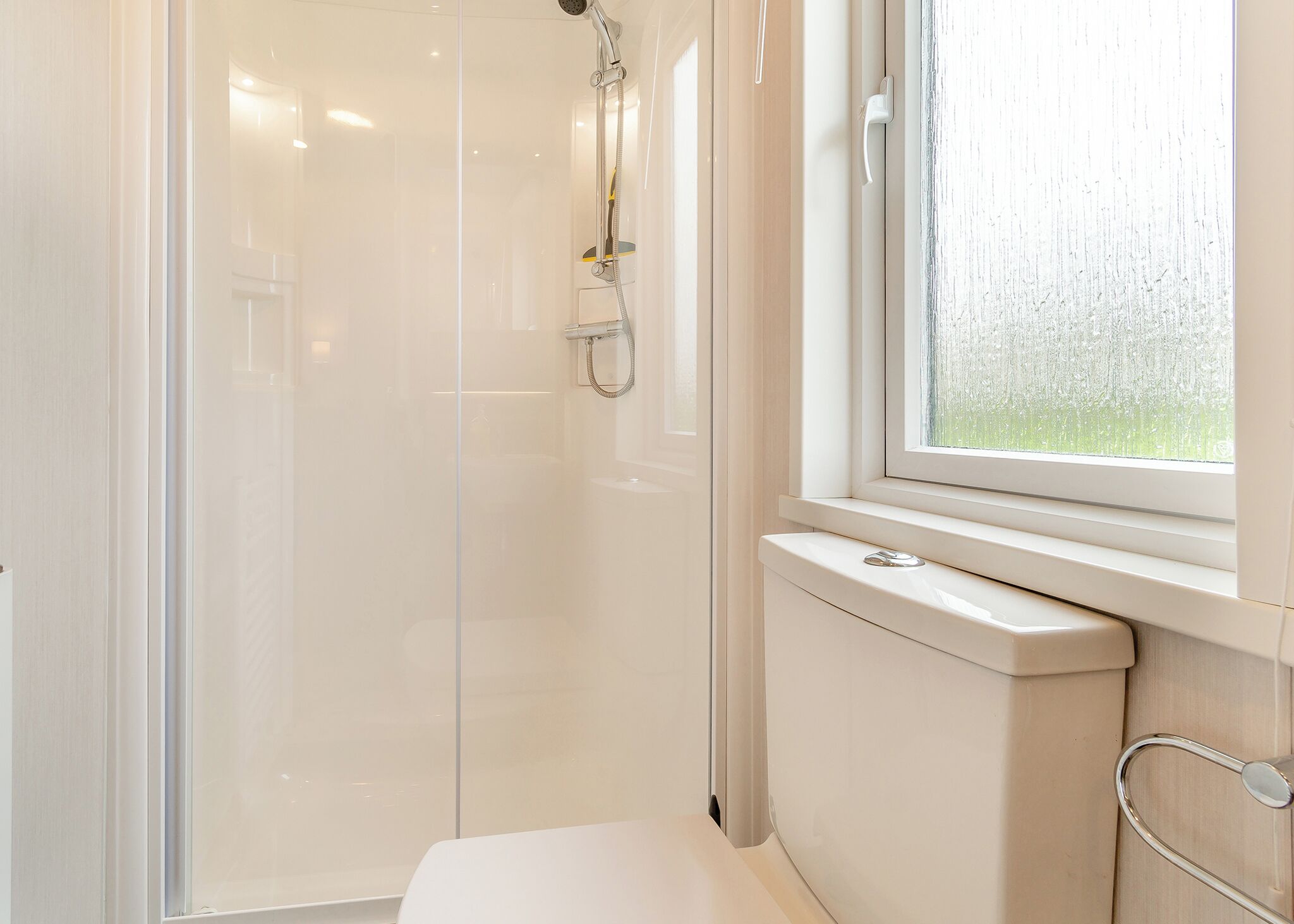 Une salle de bain moderne avec une douche à l’italienne en verre, des toilettes et une fenêtre donnant sur un beau paysage.