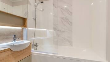 A modern bathroom with a glass-enclosed shower, a white sink, and marble tiles.