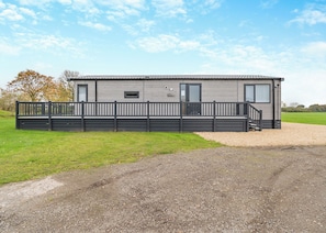 A modern, single-story mobile home with a fenced deck, a gravel driveway, and a grassy field in the background. - Family and dog friendly lodge. (Swinethorpe, Nr Lincoln)