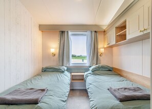 Ein Zimmer mit zwei Betten, einem Vorhangfenster, einer Wandleuchte und einem Holzschrank.