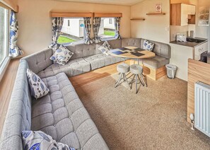 A caravan interior with a sofa set, a table with stools, a kitchen area, and a view through the windows. - 2 bedroom accommodation in New Quay (New Quay)