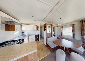 Uma cozinha compacta para motorhome com área de refeições, incluindo mesa e assentos, e um pequeno espaço para cozinha.