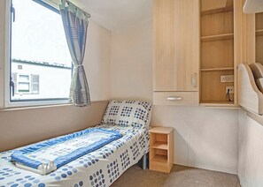A small bedroom with a single bed, a wooden cabinet, a small shelf, and a window with curtains.