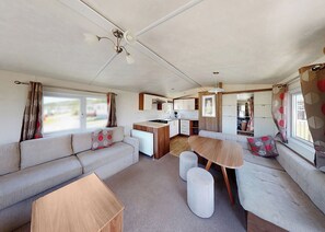 A compact RV interior with a kitchenette, a sofa, a dining table, and a ceiling fan.