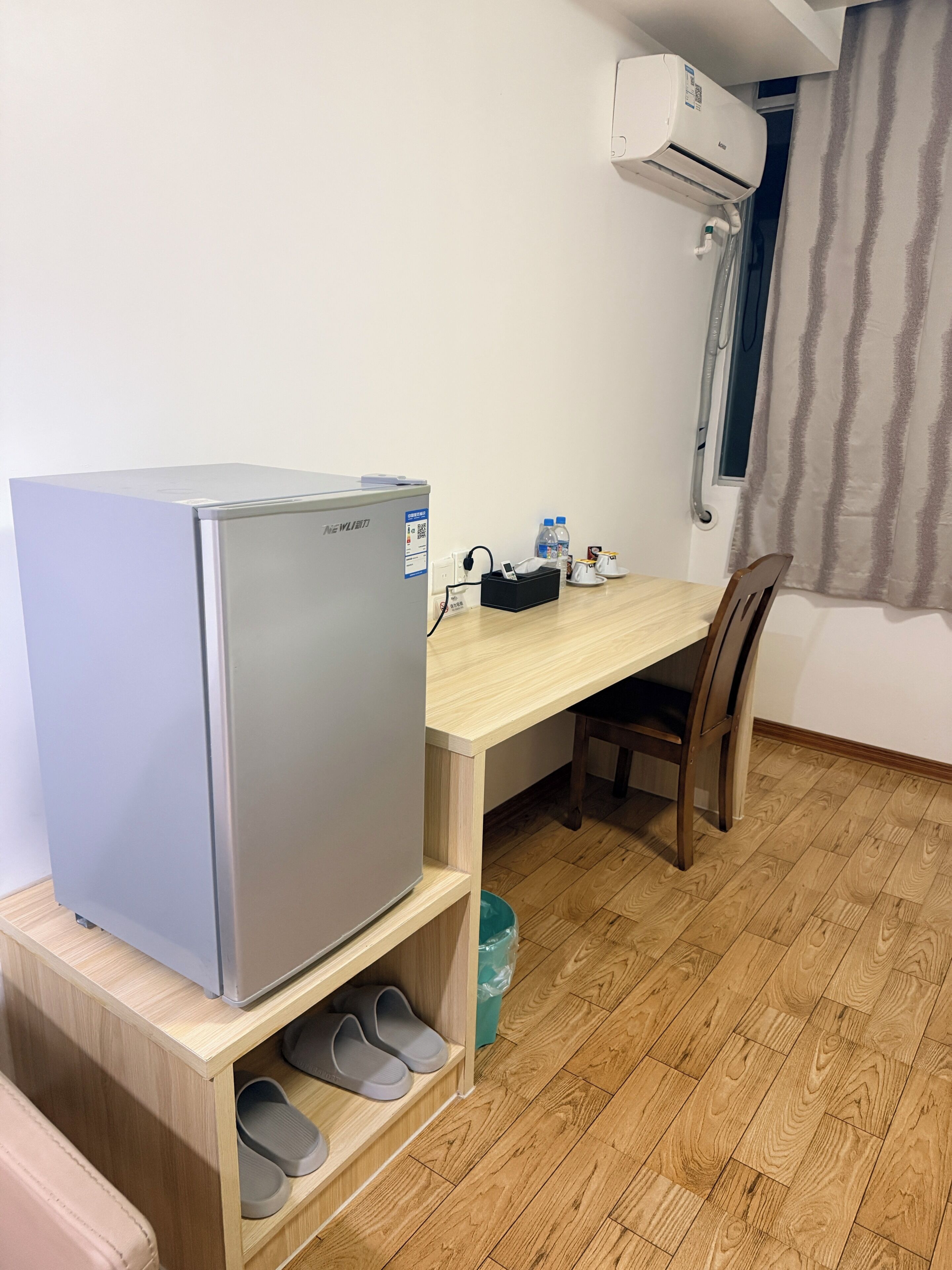 A compact kitchenette with a refrigerator, a wooden table, a chair, and a window with curtains.