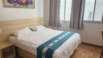 A neatly made bed with a blue and white bedspread, a wooden headboard, a nightstand, and a painting of flowers on the wall.