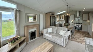A living room with a fireplace, sofa, coffee table, and a view of the outdoors. - Platinum 2 Bed Spa Slps 4 (Pet) (Clarach)