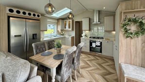 A compact kitchen with modern appliances, a dining area with a wooden table and chairs, and a herringbone-patterned floor. - Platinum 2 Bed Spa Slps 4 (Pet) (Clarach)